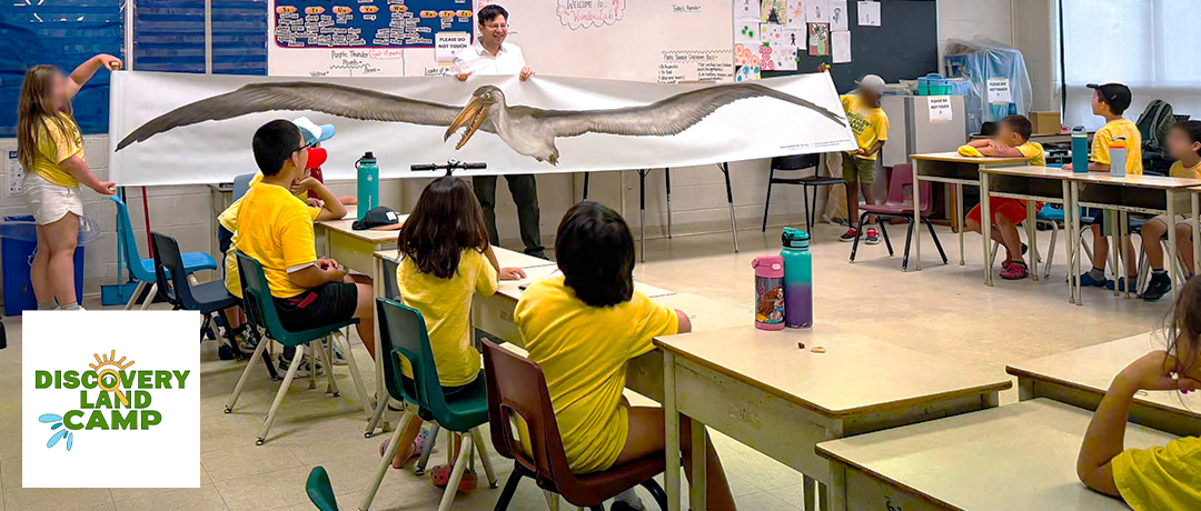 Man showing banner of life-sized Odontopteryx gigas - a huge prehistoric bird - to a group of child campers. Discovery Land Camp logo in bottom left.