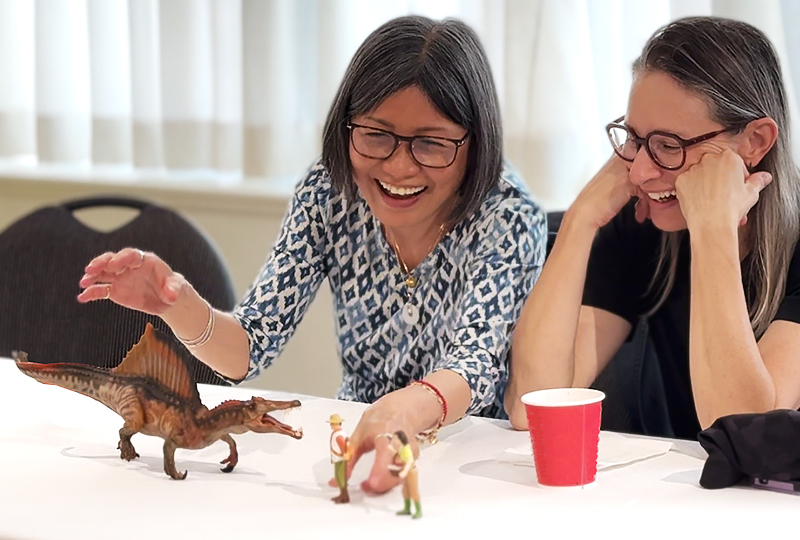 Participants playing with figurines of Spinosaurus and humans while smiling.